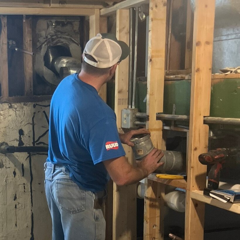 Handyman performing plumbing and ductwork repair in an Evergreen Park basement.